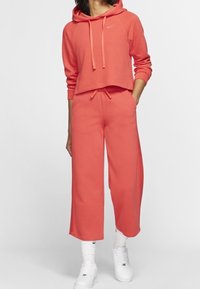 Korallfärgad randig crop-top med huva och dragsnören, tillsammans med matchande vida byxor. Vita sneakers fulländar outfiten.