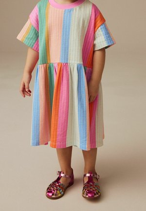Robe rayée multicolore à taille basse, manches courtes et encolure rose, associée à des sandales roses brillantes avec un motif tressé.