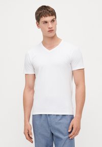 T-shirt blanc à manches courtes et col en V, fabriqué dans un tissu en coton mélangé doux, avec une coupe ajustée et un design simple et minimal.