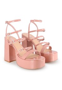 Tacones de plataforma de charol rosa con múltiples correas delgadas y detalles de hebilla, con un tacón grueso y una textura suave.