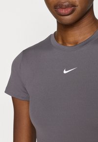 Maglietta sportiva grigia a maniche corte con scollo rotondo e piccolo logo Nike bianco sulla parte superiore sinistra del petto. Tessuto liscio ed elastico.