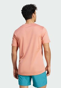 Camiseta deportiva de manga corta en color rosa, fabricada con un material ligero de textura suave, con escote redondeado y un sutil logotipo en la manga.