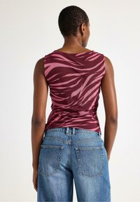 Murstangsfarvet ærmeløs top med lyserøde zebra striber, parret med lyseblå højtsiddende jeans med afslappet pasform og baglommer.