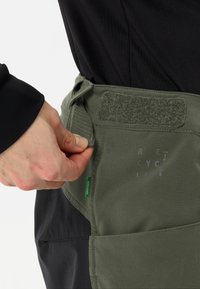 Olijfgroene stoffen taille-apron met klittenbandsluiting, voorzien van een voorkrui en geprinte tekst. Zachte textuur en duurzaam ontwerp.