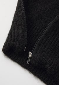 Crna pletena rubna tkanina s rebrastom teksturom, sa srebrnim zatvaračem za zatvaranje. Mekan, fluffy materijal pojačava toplinu.