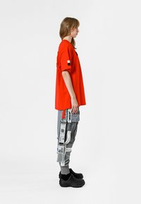 Camiseta roja de gran tamaño, pantalones de cargo grises con bolsillos laterales y zapatillas negras de textura, que muestran un ajuste relajado y detalles únicos.