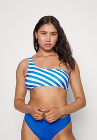 Top de bikini de um ombro em azul e branco às riscas, combinado com fundo alto azul sólido. Tecido liso e elástico com um ajuste justo.