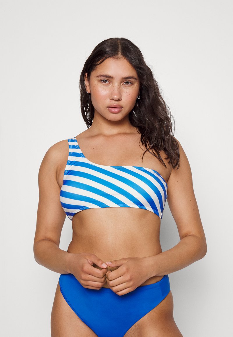 Top de bikini de um ombro em azul e branco às riscas, combinado com fundo alto azul sólido. Tecido liso e elástico com um ajuste justo.