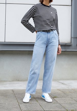 Stribet sort-hvid langærmet top, højtaljede lyseblå jeans og hvide sneakers med blå detaljer; bælte med metalskruer.