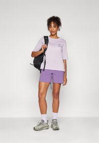Light purple t-shirt with short sleeves, paired with lavender shorts. Worn with gray hiking shoes and a black backpack.