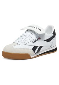 Baltas sporta apavi ar melniem akcentiem, zamšādas purngala aizsardzība un gumijas zole. Iezīmējas ar auklēm un Velcro siksnu uz mēles.