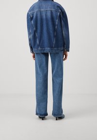 Jeansjacka och vida jeans i medelblått. Jackan har klassiska sömmar och knappdetaljer, medan jeansen har råa fållar.