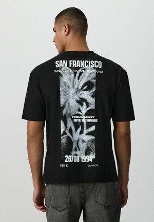 Mand iført sort T-shirt med hvidt abstrakt motiv og tekst, der henviser til San Francisco-festivalen, dato 28/08/1994 og Pier 37 som sted.