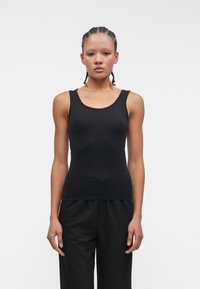 Czarna bezrękawnikowa bluzka z okrągłym dekoltem, wykonana z gładkiego, elastycznego materiału, noszona z luźnymi czarnymi spodniami.