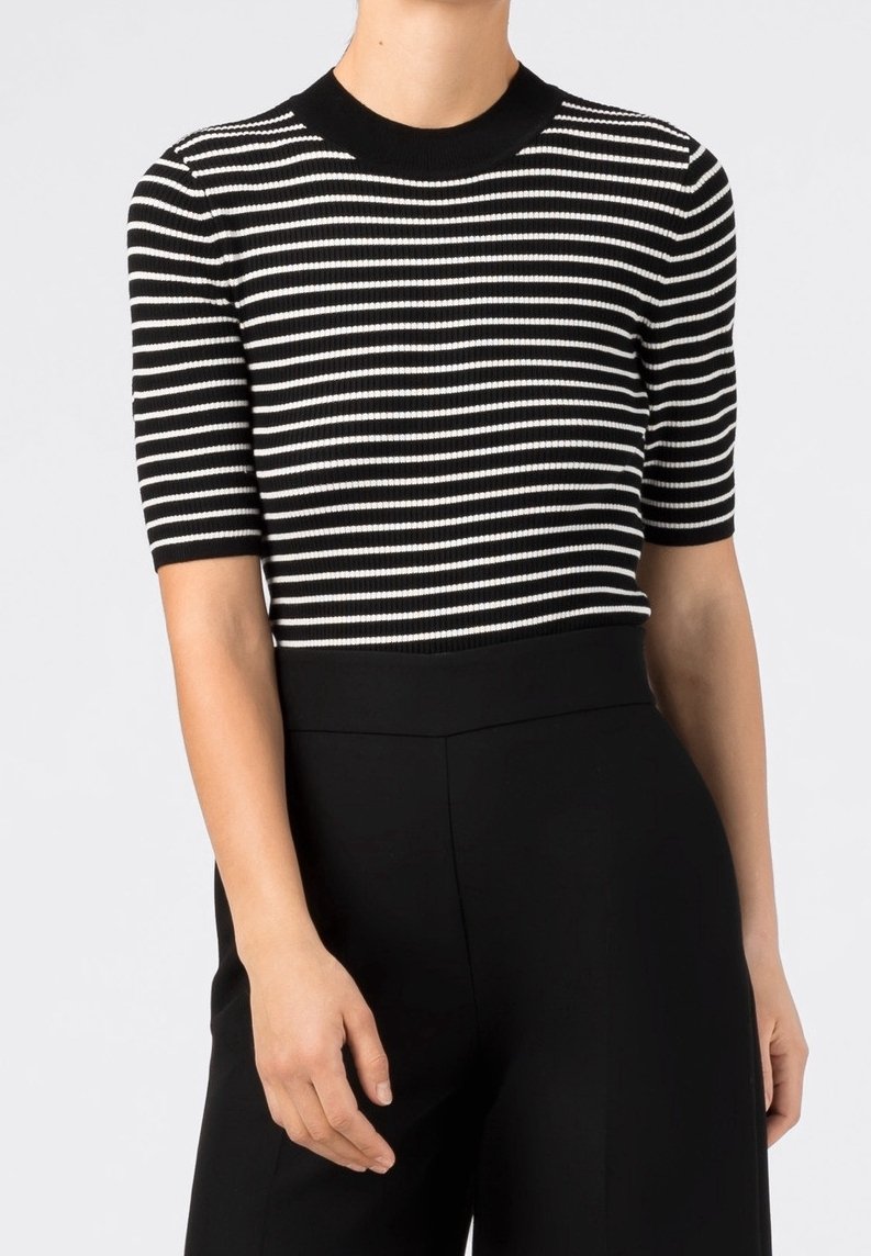 Personne portant un haut à manches courtes rayé horizontalement noir et blanc et un pantalon noir taille haute sur un fond uni.