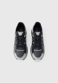 Černé sportovní boty s texturovaným vzorem, šedými prvky, bílými detaily a černými tkaničkami. Kulatá špička a polstrovaná podešev.
