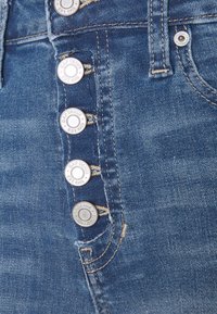 Blå denimhög midja jeans med en femknapplåsning som har silverdetaljer. Slät textur med lätt blekning och söm detaljer.