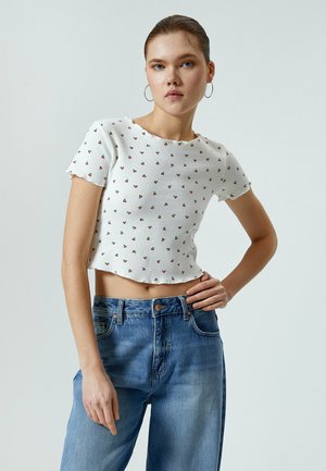 Top corto blanco acanalado con pequeños patrones triangulares rojos, que cuenta con un escote redondo y mangas cortas, combinado con unos pantalones vaqueros de tiro alto en azul claro.