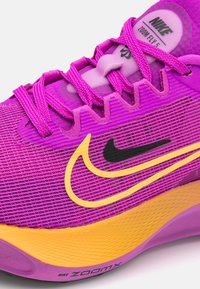 Běžecká obuv Nike Zoom Fly 5 v živé fialové barvě s žlutým akcentem a černým logem. Obsahuje texturovaný svršek a polstrovaný jazyk, navržena pro výkon.