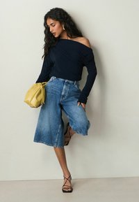 Námořnická off-shoulder halenka s dlouhými rukávy, vysoké džíny culottes, černé sandály na pásky a žlutá taška na stahování.