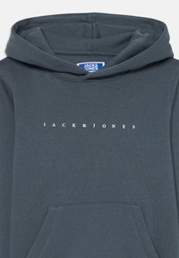 Sötét teal színű kapucnis pulóver sima anyagból, elülső zsebbel és kapucnival. A "JACK & JONES" márkanevének fehér betűkkel nyomtatva a mellkason.