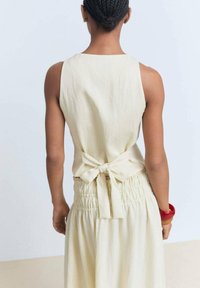 Cremfarbendes Leinenkleid mit tailliertem Oberteil und gerafftem Bund. Mit Schleifendetail hinten, das eine glatte Textur und ein minimalistisches Design aufweist.