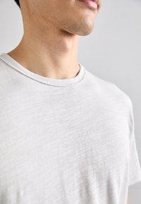 T-shirt di cotone grigio chiaro con scollatura rotonda, maniche corte e una consistenza morbida e liscia. Design minimalista senza motivi visibili.