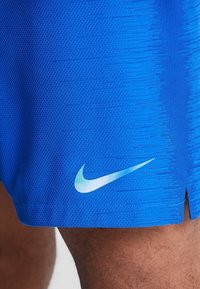 Pantalones deportivos azules hechos de tela texturizada, con un logo de Nike en azul claro en la parte inferior izquierda y una abertura lateral para mayor movilidad.