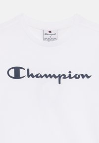 Bílá bavlněná tričko s výrazným námořnickým logem "Champion" na přední straně, s kulatým výstřihem a standardními krátkými rukávy.