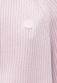 Gaiši rozā adīts džemperis ar teksturētu rakstu un nelielu apaļu logotipu sānos. Viegls materiāls un brīvs piegriezums.