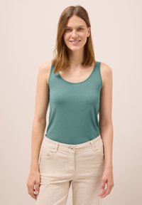 Teal tank top made of soft, stretchy fabric, featuring a rounded neckline and thin straps, paired with light-colored, fitted pants.