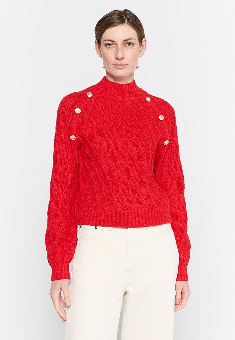 Pullover rosso lavorato a maglia con collo alto, motivo a treccia e orlo a costine. Presenta dettagli in argento sui bottoni delle spalle.