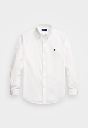 Vit långärmad skjorta i bomull, med krage med knappar, framför knappslå och en liten marinblå logotyp på vänster bröst.