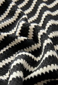 Tkanina s černobílým zigzag vzorem, se strukturovaným, tkaným vzhledem, zobrazuje jemné vlákna a viditelné texturové variace.