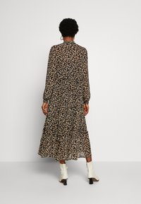 Pitkä musta mekko beige kukkakuviolla, jossa on kerrokselliset röyhelöt, pitkät hihat ja korkea kaulus. Yhdistetty valkoisiin korkokenkisiin nilkkakenkiin.