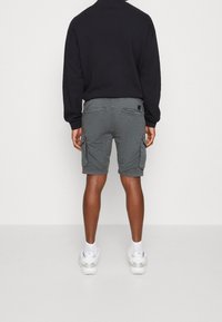 Shorts cargo gris avec poches latérales et un petit logo, associés à un sweatshirt noir et des baskets blanches. Design simple et fonctionnel.