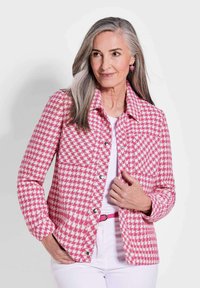 Roze en witte houndstooth-gepatroneerde jack met een kraag, voorzakken en zilveren knoopsluitingen, gedragen over een witte top.