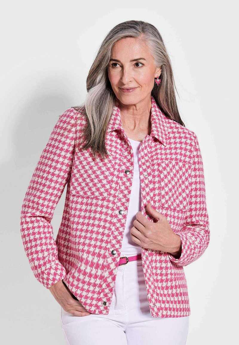 Roze en witte houndstooth-gepatroneerde jack met een kraag, voorzakken en zilveren knoopsluitingen, gedragen over een witte top.