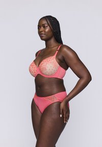 Korallinvärinen alusvaatesetti, joka sisältää kuviollisen pitsibra ja sileän alusosan, esittelee monimutkaisia yksityiskohtia ja kontrastisia tekstuureja.