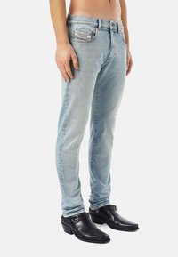 Light blue denim jeans with a slim fit, subtle fading, five-pocket design, and a contrasting label. Paired with black leather ankle boots.