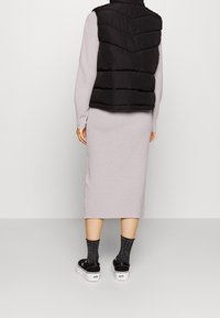 Černá prošívaná vesta s chevronovým prošíváním přes světle šedé šaty s dlouhým rukávem. Nošena s černými botami na platformě a šedými texturovanými ponožkami.