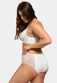Ensemble de bralette blanche et de culotte taille haute avec des panneaux en dentelle florale, tissu lisse et bretelles réglables. Vue de côté avec un modèle.