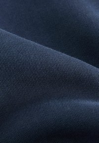 Tissu bleu marine avec une texture lisse et un motif tricoté fin, montrant de subtiles variations de couleur et de lumière à la surface.