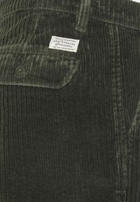 Mörkgrön kordflorsbyxa med en ficka med knappslå och en vit Levi Strauss-märkesetikett ovanför fickan.