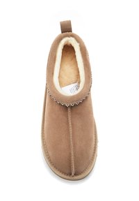 Pantofole in scamosciato marrone con morbida fodera in pelliccia color crema, punta arrotondata e bordo decorativo cucito. Include una linguetta per indossarle facilmente.