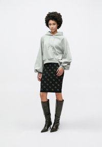 Γκρι φούτερ με κουκούλα και κορδόνι, σε συνδυασμό με μαύρη στενή φούστα με σχέδια και καφέ δερμάτινες μπότες μέχρι το γόνατο.