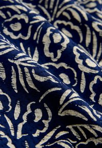 Merekangast tumesinisel toonil, millel on tekstuuriga lillemuster kreemjavalges värvitoonis, millel on keerukad lehed ja õied, millel on nähtav läige ja sügavus.