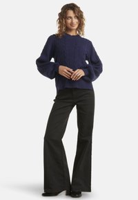 Navy cable-knit sweater with balloon sleeves paired with high-waisted black flared jeans and black ankle boots. Smooth texture, casual design.