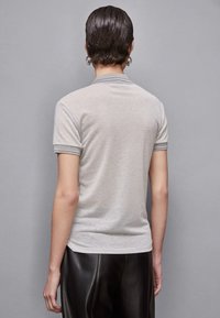 Polo grigio con maniche corte, caratterizzato da un colletto e dei polsini a costine in contrasto. Tessuto morbido, forma aderente e dettagli minimi.