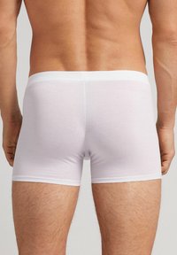 Boxers ajustados de algodón blanco con una suave banda elástica en la cintura. Diseño ceñido, textura suave y longitud hasta medio muslo, sin patrones visibles.